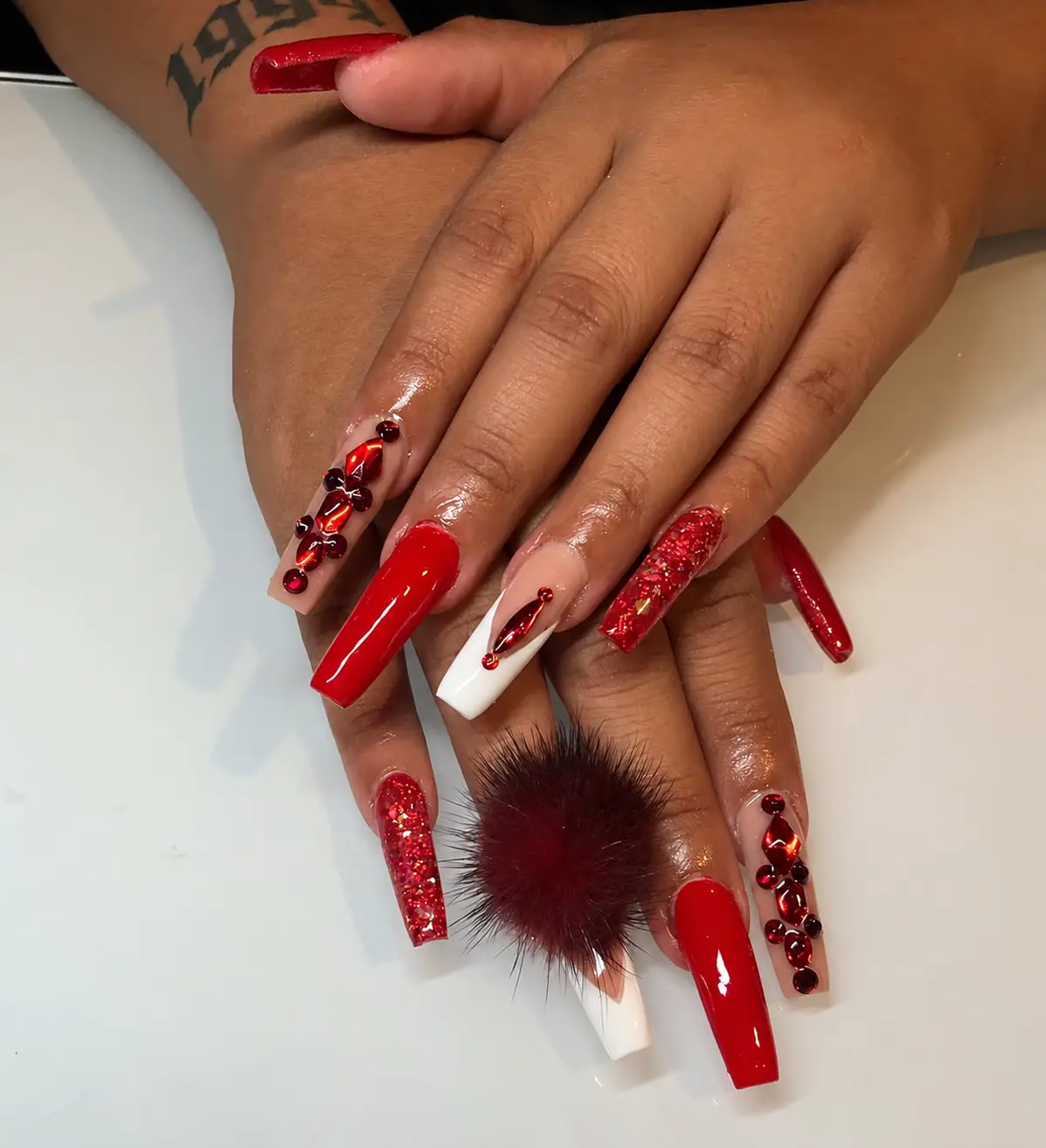 Long red and white nails with red gems, glitter and a burgundy pompom