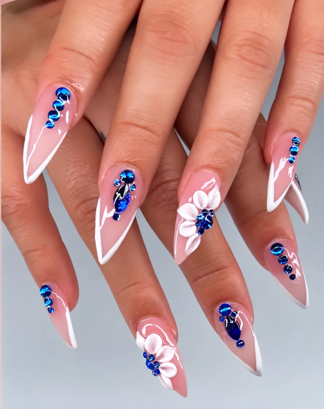 Pink stiletto nails with white outlines, blue crystals and white flowers